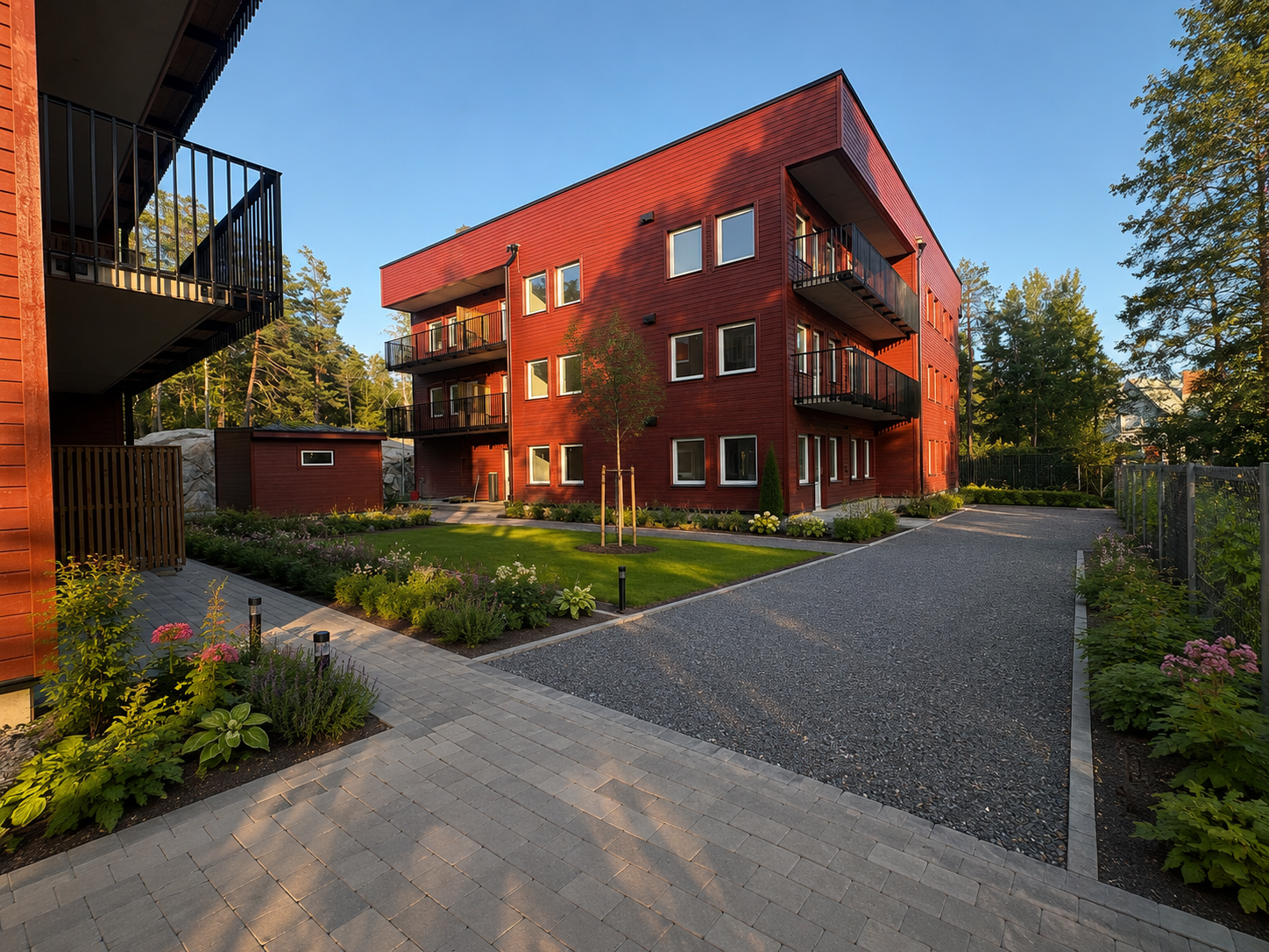 Himmelsbodavägens röda flerfamiljshus med trädgård och uppfart i kvällssol